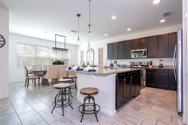 kitchen with a kitchen breakfast bar, an island with sink, dark brown cabinetry, pendant lighting, and appliances with stainless steel finishes