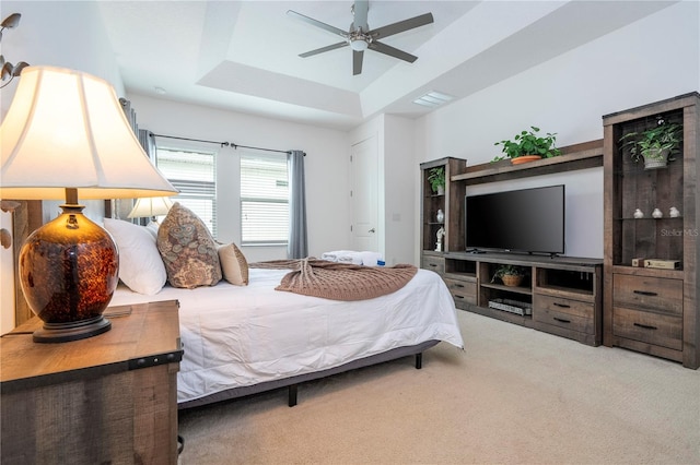 carpeted bedroom with ceiling fan and a raised ceiling