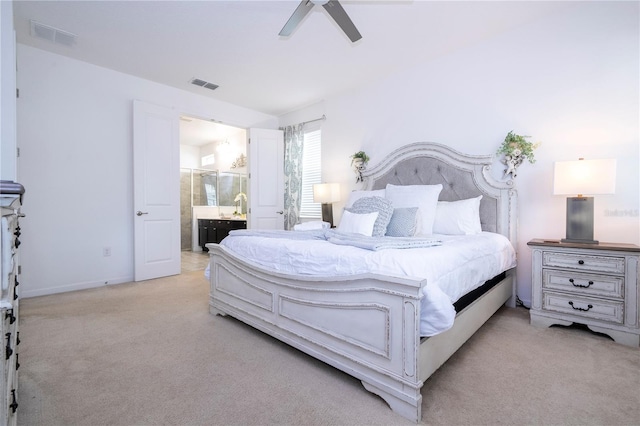 bedroom with ceiling fan, light colored carpet, and ensuite bath