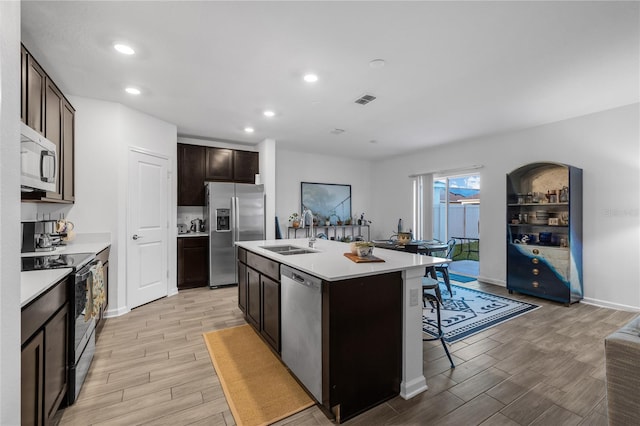 kitchen featuring sink, an island with sink, light hardwood / wood-style floors, stainless steel appliances, and a breakfast bar area