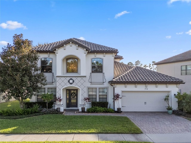 mediterranean / spanish house with a garage, a tiled roof, decorative driveway, a front lawn, and stucco siding