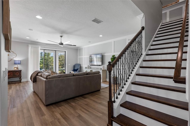 living area with stairway, a textured ceiling, visible vents, and wood finished floors