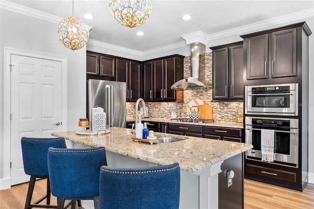 kitchen featuring appliances with stainless steel finishes, decorative light fixtures, an island with sink, and wall chimney exhaust hood