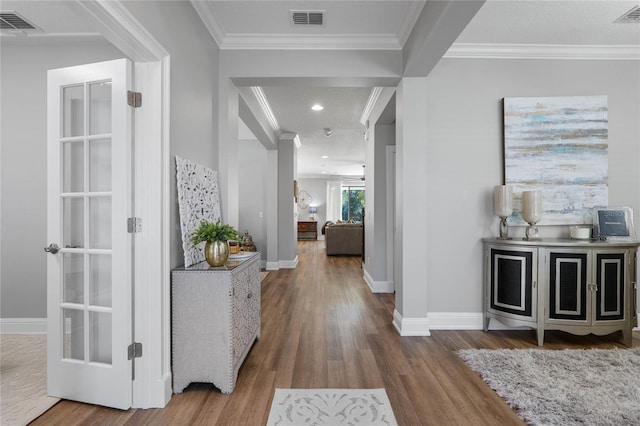 corridor featuring ornamental molding, wood finished floors, visible vents, and baseboards