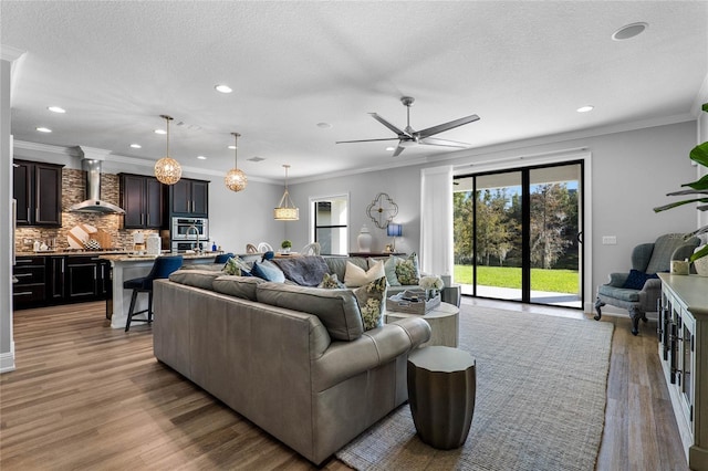 living area with light wood-type flooring, ornamental molding, a textured ceiling, and recessed lighting