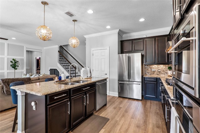 kitchen featuring a sink, open floor plan, appliances with stainless steel finishes, an island with sink, and pendant lighting