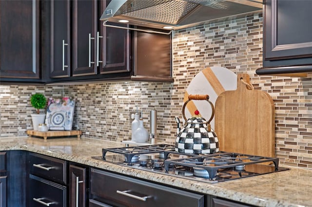 kitchen with light stone countertops, custom range hood, stainless steel gas cooktop, and decorative backsplash