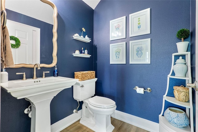 half bath featuring a sink, wood finished floors, toilet, and baseboards