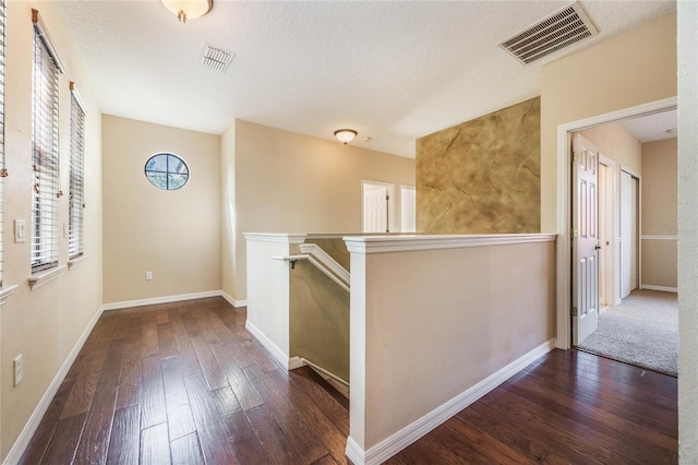 corridor with a textured ceiling and dark hardwood / wood-style flooring