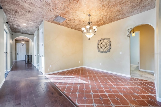 empty room featuring a chandelier, dark hardwood / wood-style floors, and a textured ceiling