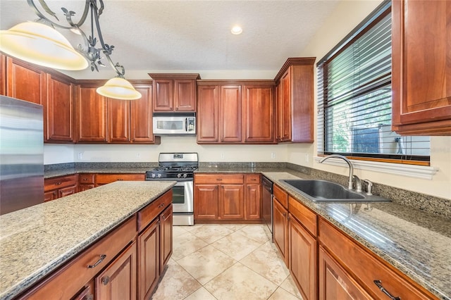 kitchen featuring sink, a textured ceiling, stainless steel appliances, pendant lighting, and dark stone countertops