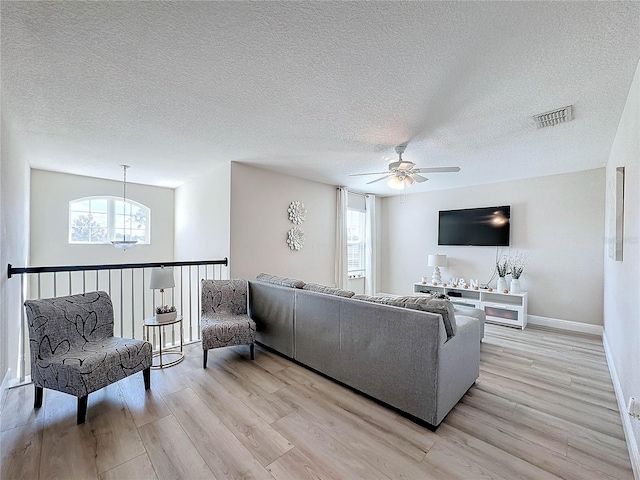 living room with ceiling fan with notable chandelier, light wood-type flooring, and a textured ceiling