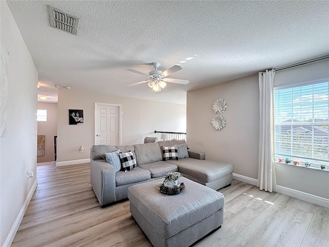 living room featuring ceiling fan, light hardwood / wood-style flooring, and a textured ceiling