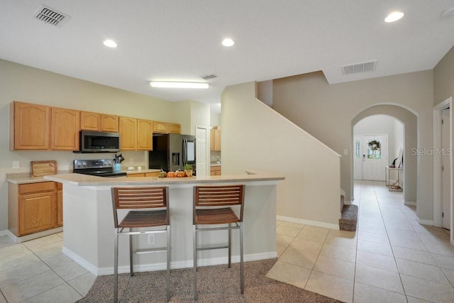 kitchen featuring appliances with stainless steel finishes, a center island, a kitchen bar, and light tile patterned floors