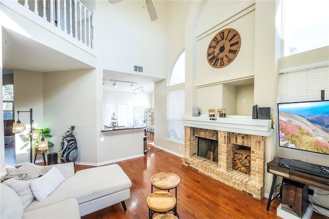 living room with a high ceiling, ceiling fan, hardwood / wood-style floors, and a fireplace