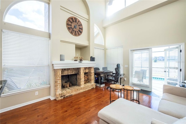 living room with wood-type flooring, a brick fireplace, and a high ceiling