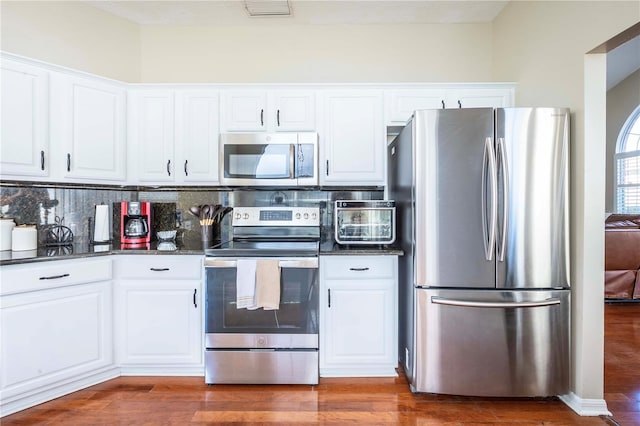 kitchen featuring stainless steel appliances, tasteful backsplash, dark wood-type flooring, and white cabinets