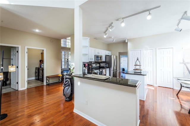 kitchen with washing machine and clothes dryer, white cabinetry, dark hardwood / wood-style flooring, kitchen peninsula, and stainless steel appliances