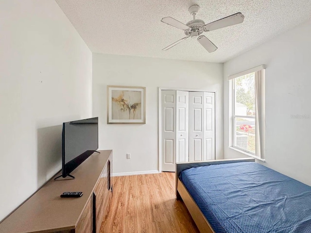 bedroom with a closet, light hardwood / wood-style flooring, ceiling fan, and a textured ceiling