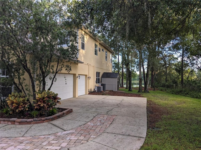 view of home's exterior with an attached garage, central AC, driveway, a yard, and stucco siding