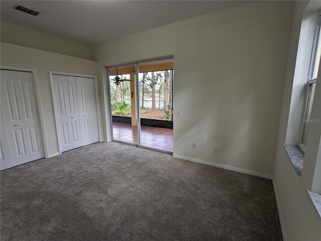 unfurnished bedroom featuring visible vents, baseboards, multiple closets, access to exterior, and dark carpet