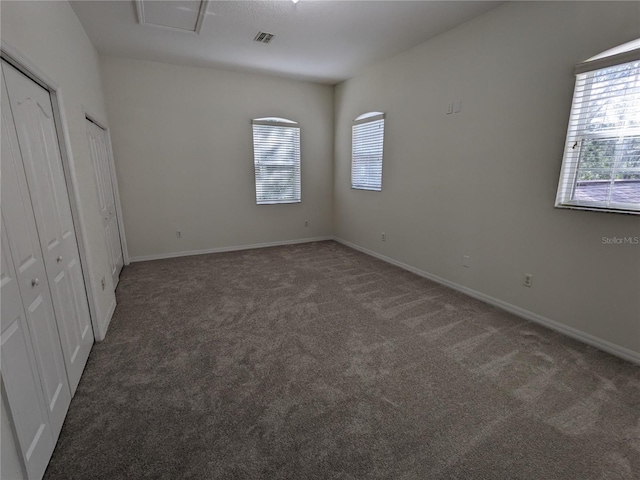 unfurnished bedroom with baseboards, visible vents, dark colored carpet, and multiple closets