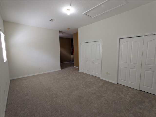 unfurnished bedroom with two closets, visible vents, attic access, carpet flooring, and baseboards