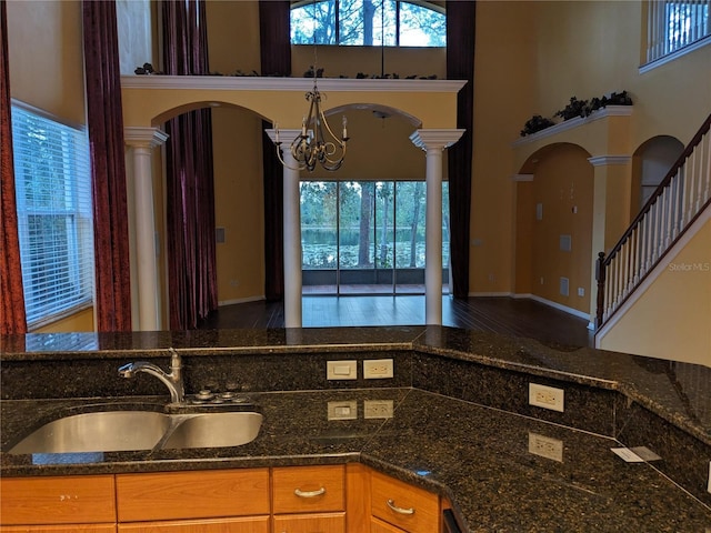 kitchen with arched walkways, a high ceiling, open floor plan, a sink, and dark stone counters