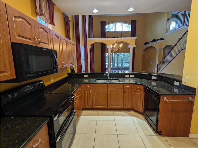 kitchen featuring light tile patterned floors, dark stone counters, brown cabinets, black appliances, and a sink