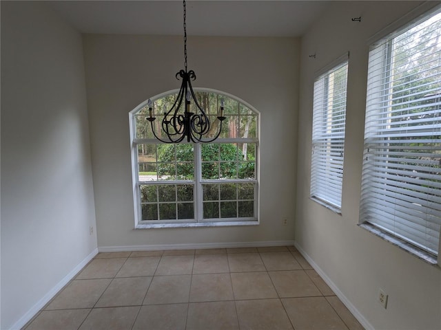 unfurnished dining area with an inviting chandelier, light tile patterned floors, and baseboards