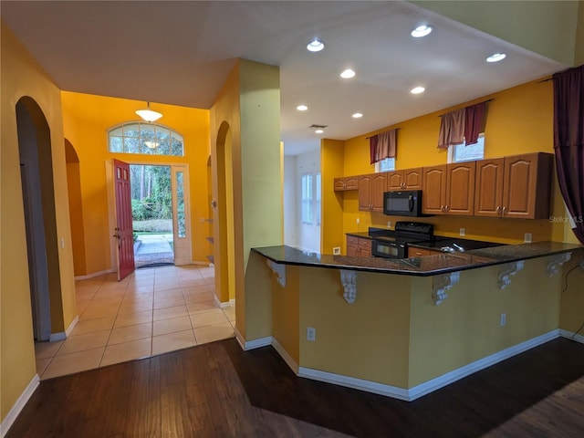 kitchen with light wood finished floors, arched walkways, brown cabinets, a peninsula, and black appliances