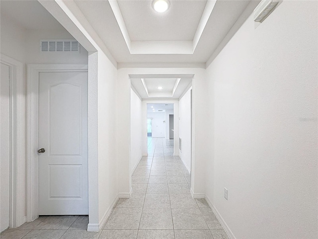 hallway with light tile patterned floors and a tray ceiling