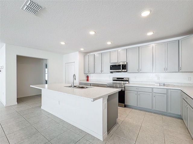 kitchen featuring light tile patterned floors, an island with sink, a textured ceiling, sink, and stainless steel appliances