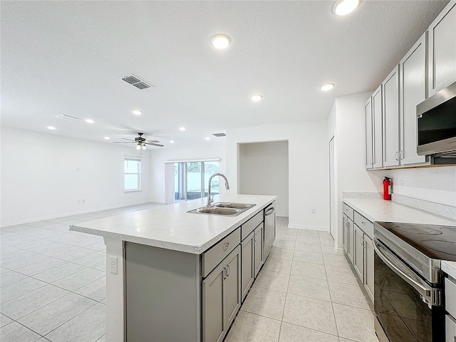 kitchen with a kitchen island with sink, stainless steel appliances, sink, gray cabinets, and ceiling fan