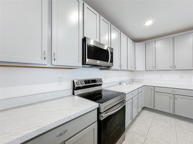 kitchen featuring stainless steel appliances, a textured ceiling, light tile patterned flooring, and gray cabinets