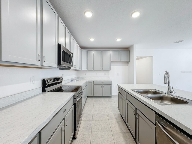 kitchen featuring appliances with stainless steel finishes, a textured ceiling, light tile patterned flooring, gray cabinetry, and sink