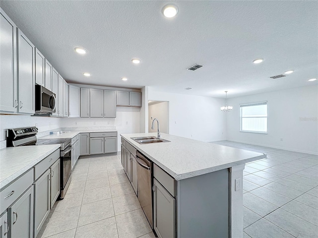 kitchen featuring a kitchen island with sink, gray cabinetry, stainless steel appliances, sink, and a notable chandelier