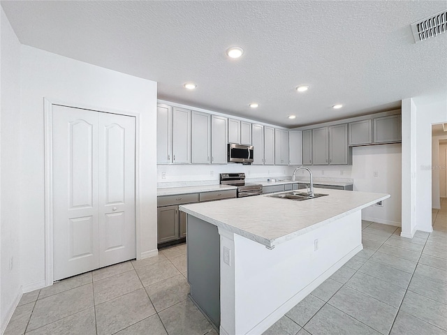 kitchen featuring a center island with sink, sink, light tile patterned floors, appliances with stainless steel finishes, and a textured ceiling