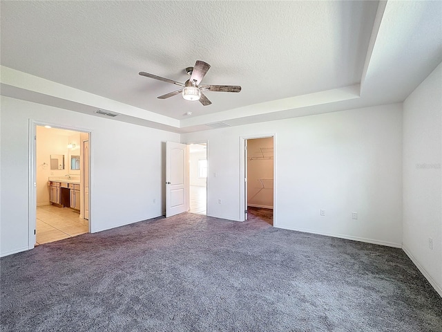 unfurnished bedroom with ceiling fan, a textured ceiling, a spacious closet, a closet, and light colored carpet