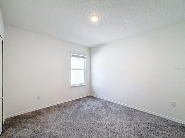 spare room featuring a textured ceiling and dark carpet