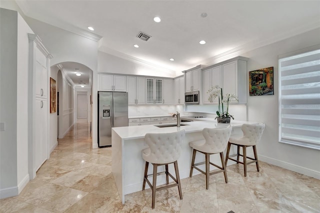 kitchen with a breakfast bar area, stainless steel appliances, ornamental molding, sink, and vaulted ceiling