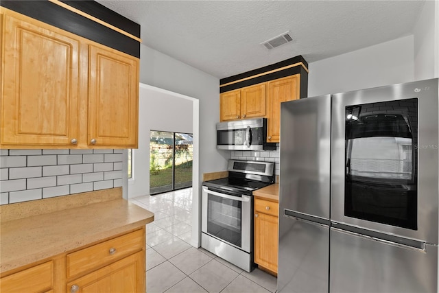 kitchen with stainless steel appliances, light tile patterned floors, light brown cabinetry, a textured ceiling, and tasteful backsplash