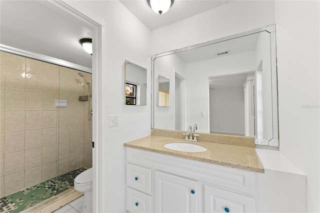 bathroom with toilet, vanity, tile patterned floors, and tiled shower