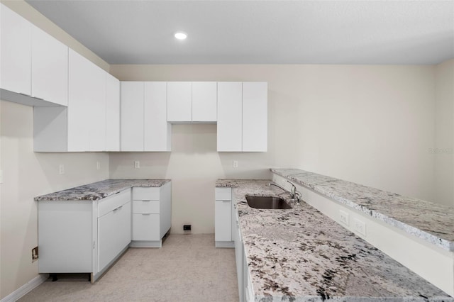 kitchen featuring light stone countertops, sink, white cabinets, and light colored carpet