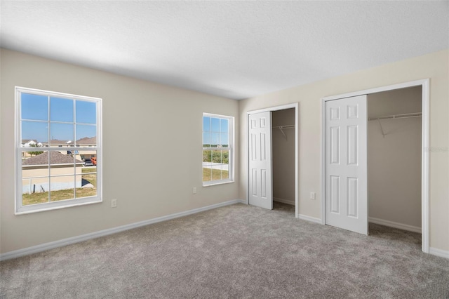 unfurnished bedroom featuring multiple closets, a textured ceiling, and light colored carpet