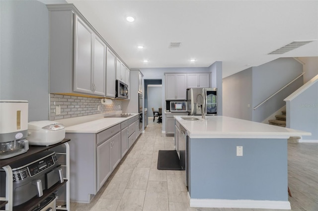 kitchen featuring visible vents, decorative backsplash, an island with sink, appliances with stainless steel finishes, and gray cabinetry