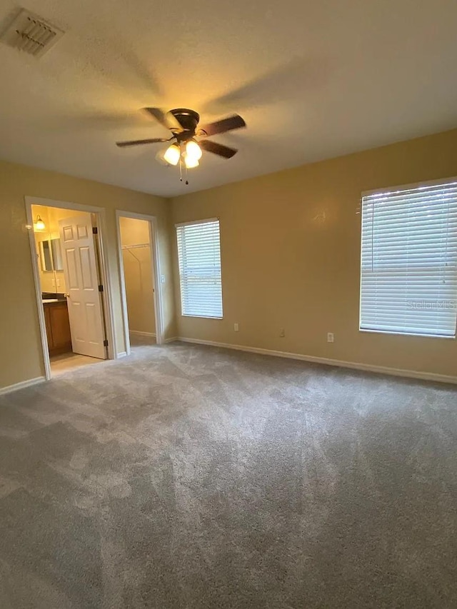 unfurnished bedroom featuring a spacious closet, ceiling fan, connected bathroom, and carpet