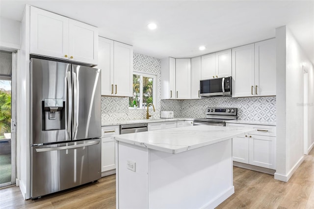 kitchen with light hardwood / wood-style floors, stainless steel appliances, a kitchen island, and white cabinets