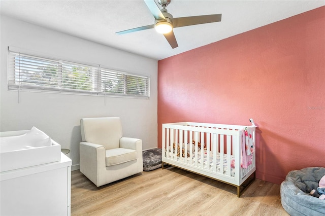 bedroom with a nursery area, light wood-type flooring, and ceiling fan