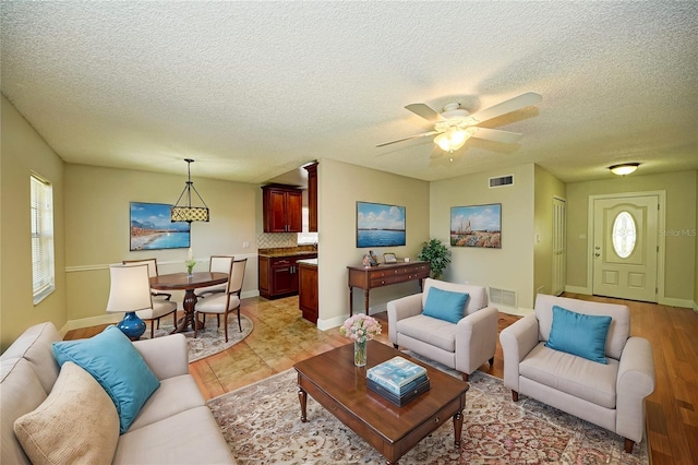 living room with a textured ceiling, light wood-type flooring, and ceiling fan